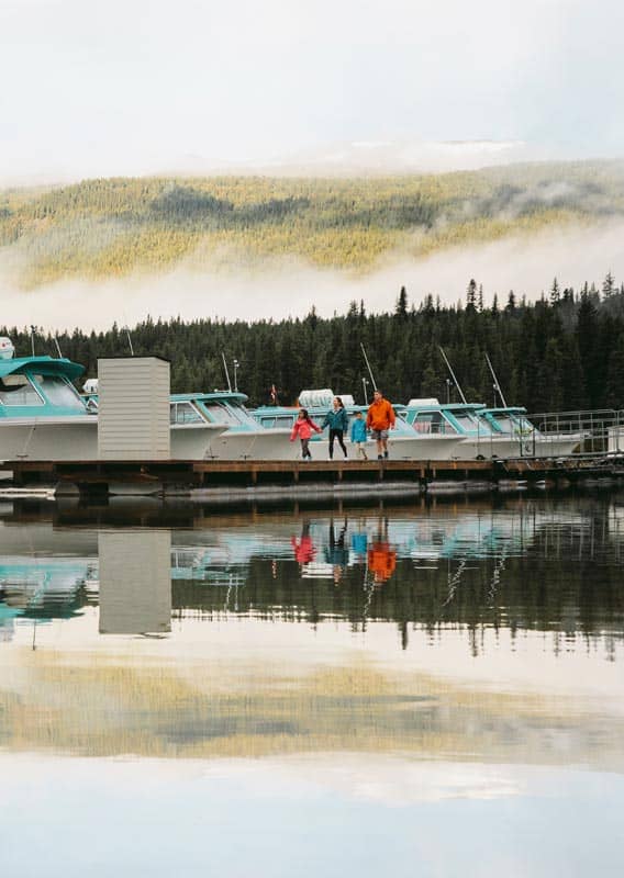 A family walks on a dock next to white and blue boats.