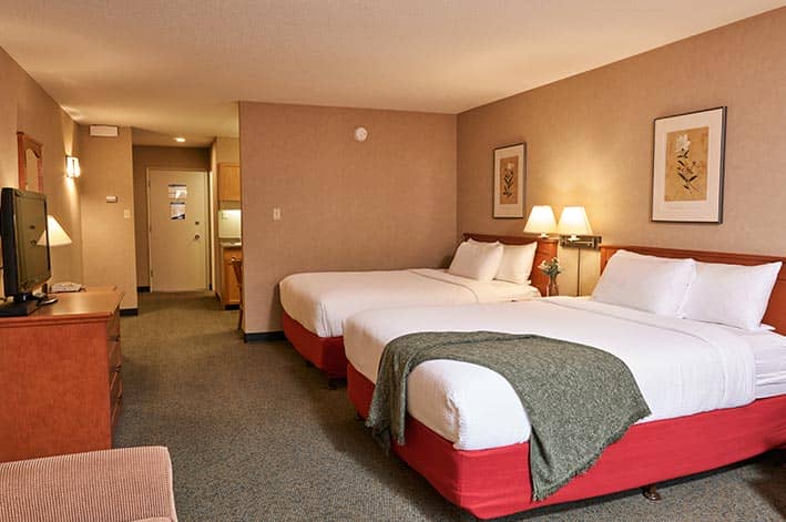 A hotel room interior, with view of two beds, edge of the kitchen and front door