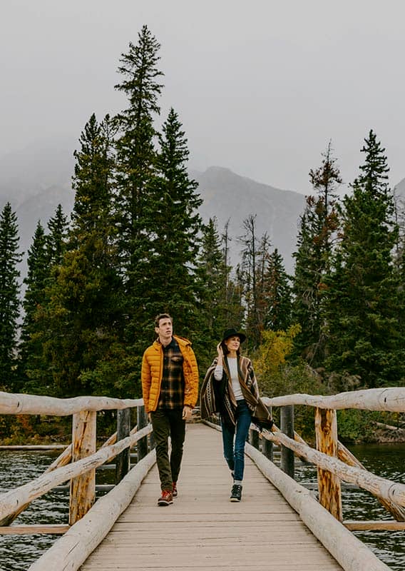 Two people walk across a small wooden bridge away from a tree-covered island.