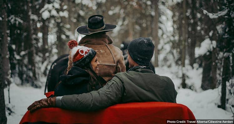 Two people ride a horse-drawn sleigh in a snowy forest.