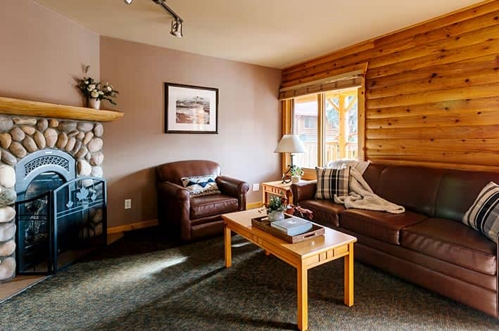 The living area of a wooden cabin with leather sofas next to a stone fireplace