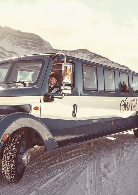 Guests and a tour guide stand outside with a historic vehicle parked next to them.