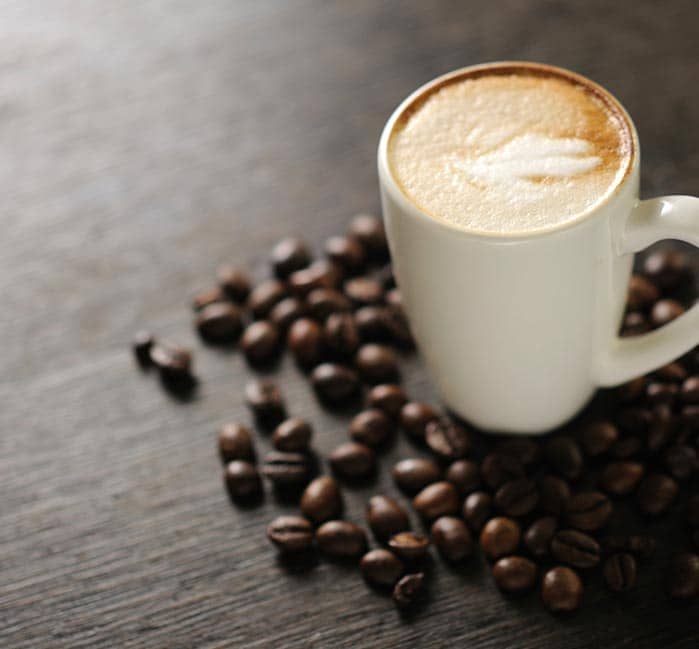  mug of foamy coffee on a table covered with coffee beans.