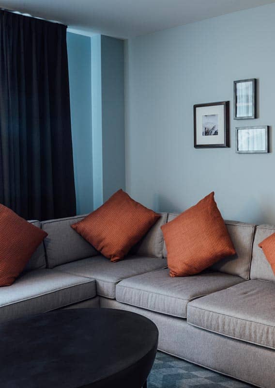 A corner couch in a hotel room with a bed in an adjacent room.