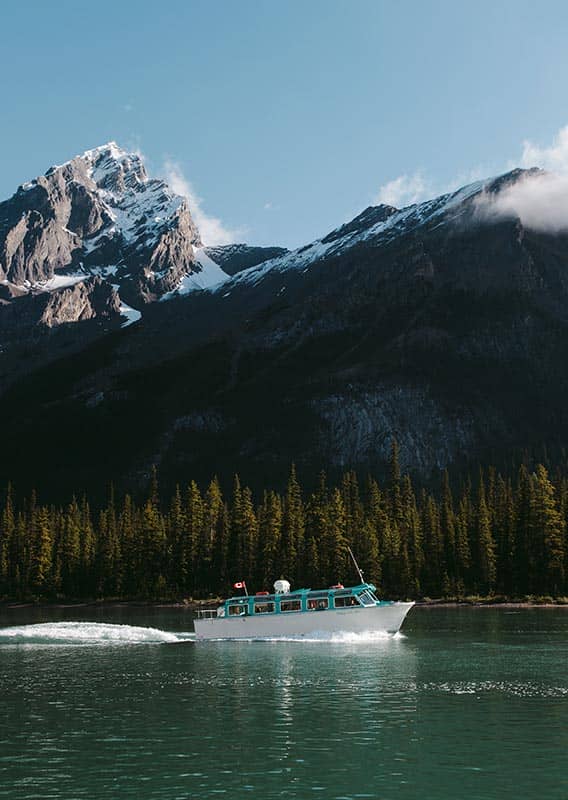 A boat cruises along a lake below forested mountainsides.