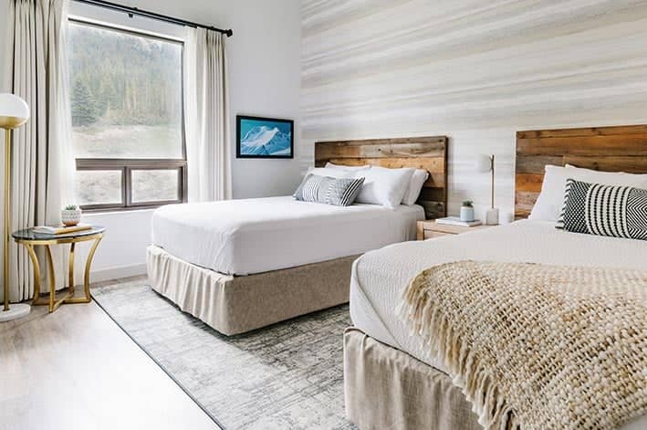 Two beds in a hotel room with a large window overlooking a forest.