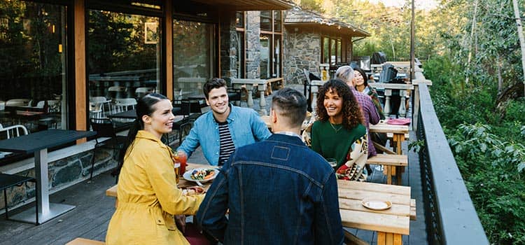 Friends sit at a picnic table on a patio smiling and laughing