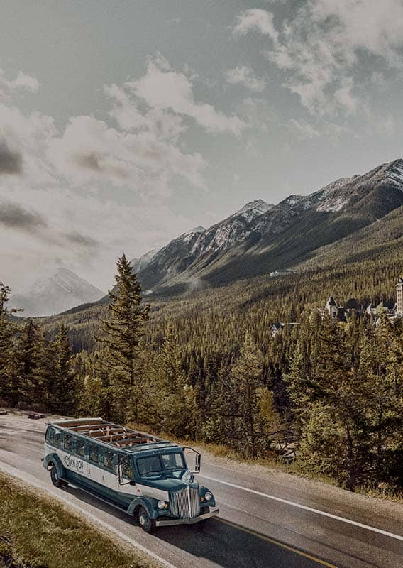 A historic style bus driving along a road among forests and mountains