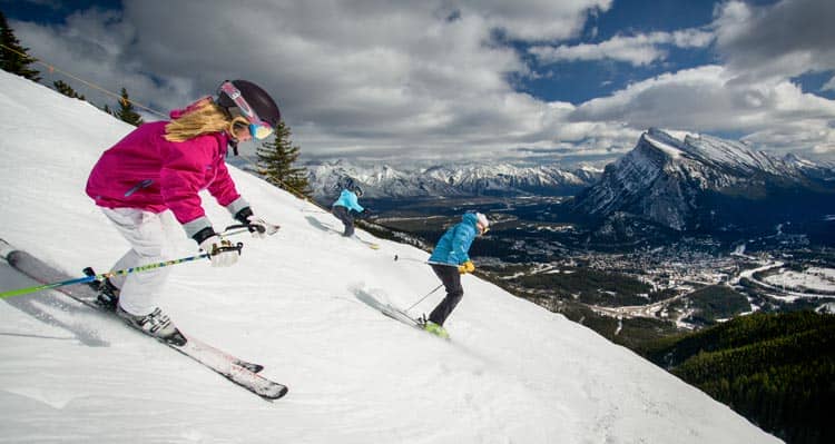 A group of skiiers go down a steep mountain.