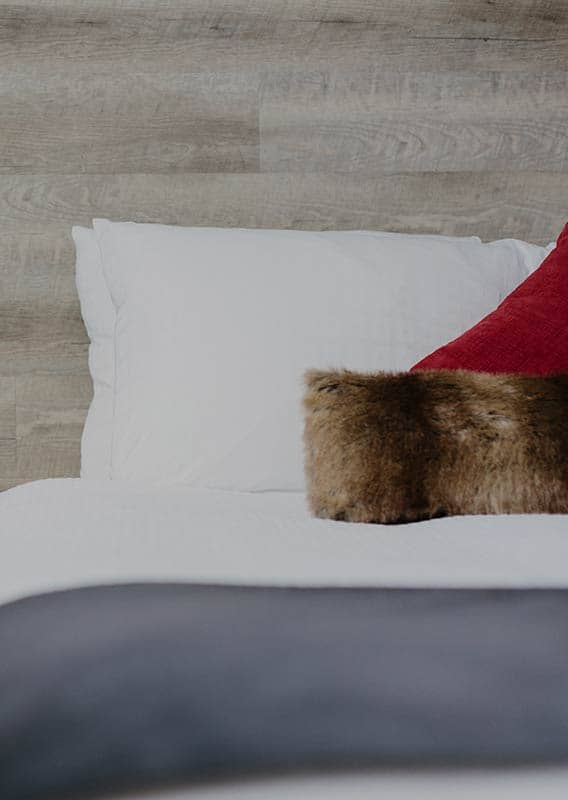 A bed with white blankets with a side table that has a book and pinecone on it.