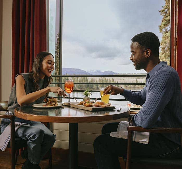 People sitting at dining tables near a large window overlooking a lake.