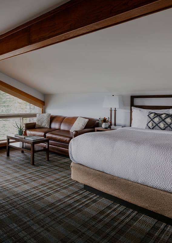 A hotel room with a king bed and a lounge area next to a large window.