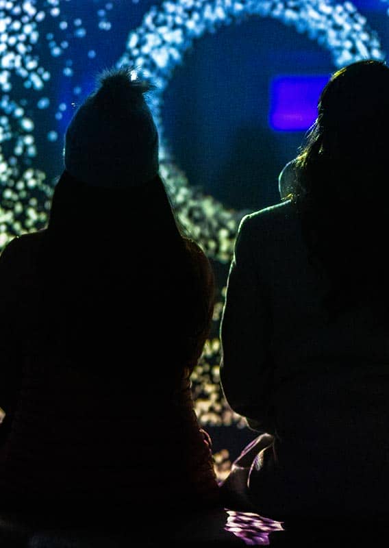 Two people sit, watching a light installation.