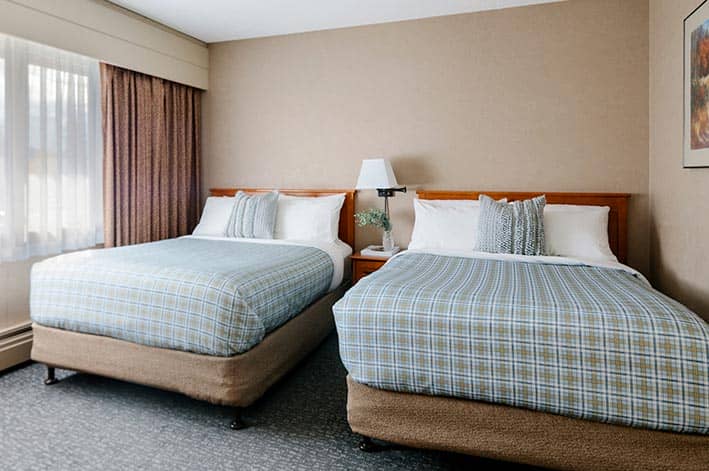 Two beds in a hotel room next to a wide window