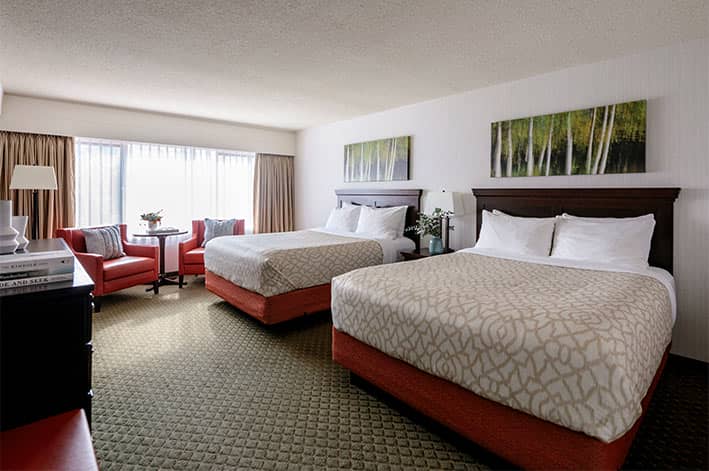 Two queen beds in a hotel room with colourful art above the headboard.