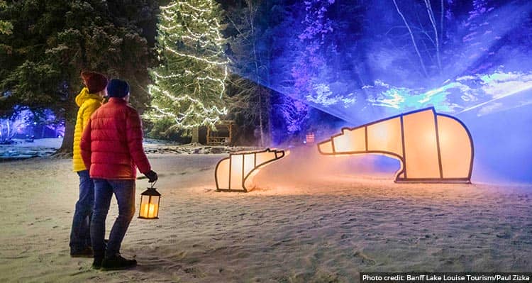 Two people watch a light art installation in a snowy park.