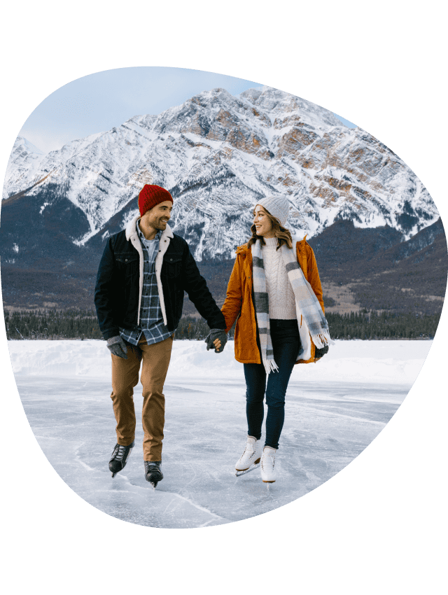 Two people hold hands, ice skating on a frozen lake.